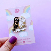 Enamel pin of a black owl representing night cuddling with a white owl representing day on packaging