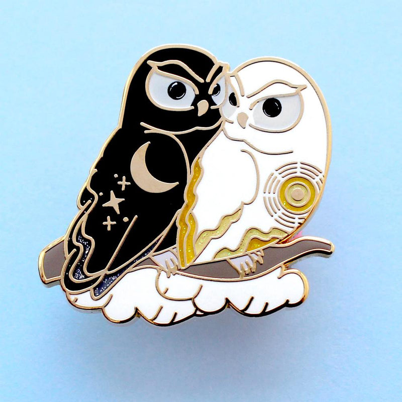 Enamel pin of a black owl representing night cuddling with a white owl representing day