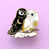 Enamel pin of a black owl representing night cuddling with a white owl representing day